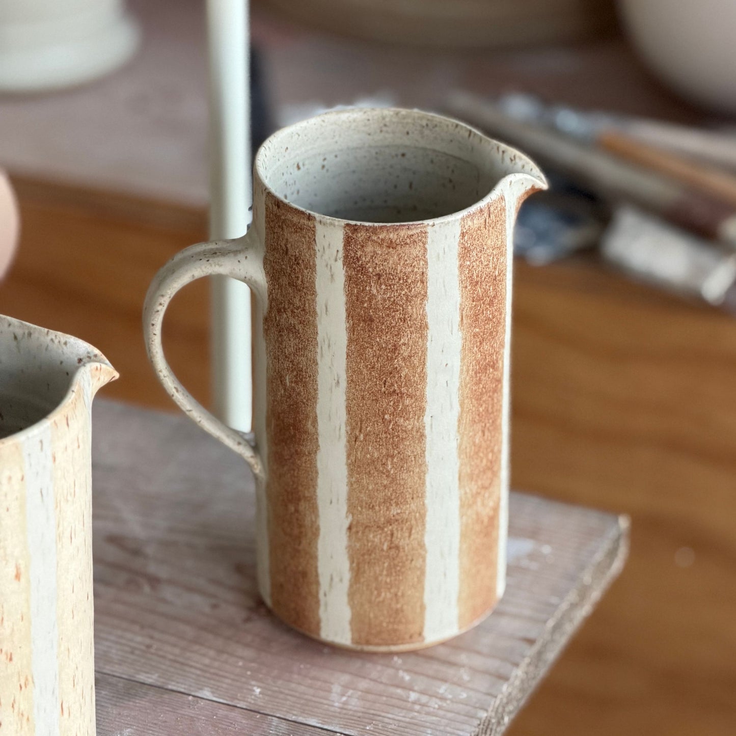Handgjord randig keramikkanna i brun glasyr på havrefärgad botten från Paradisverkstaden, cirka 20 cm hög.