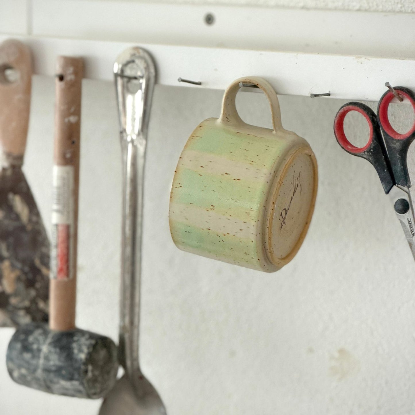 randig kopp i keramik hänger på en krok i verkstaden